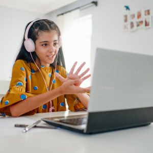 Teenage girl with headphones and laptop having online school class at home