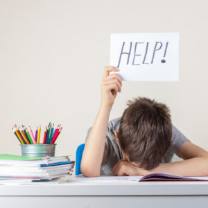 Child working on homework puts up a sign with the word "HELP!" written on it.